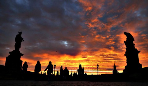 People cross the medieval Charles Bridge as the sun rises in Pra